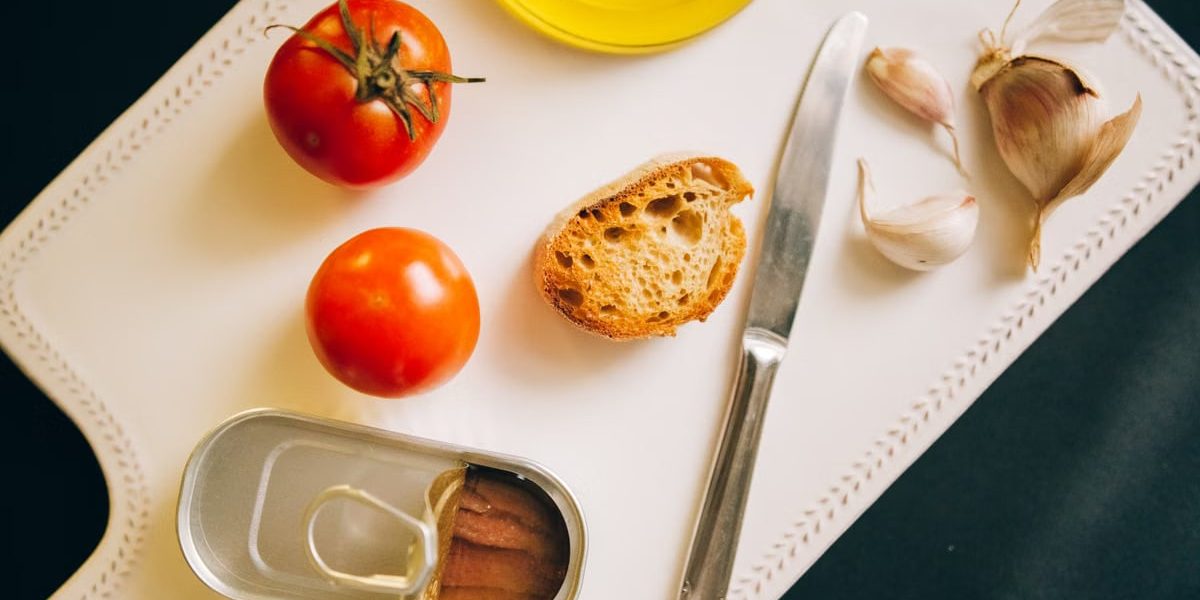 Tomatoes, bread, and sardines arranged for Catalán toast preparation.