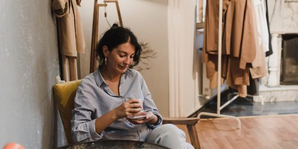 Woman sitting in a boutique, enjoying a coffee with clothes displayed nearby.